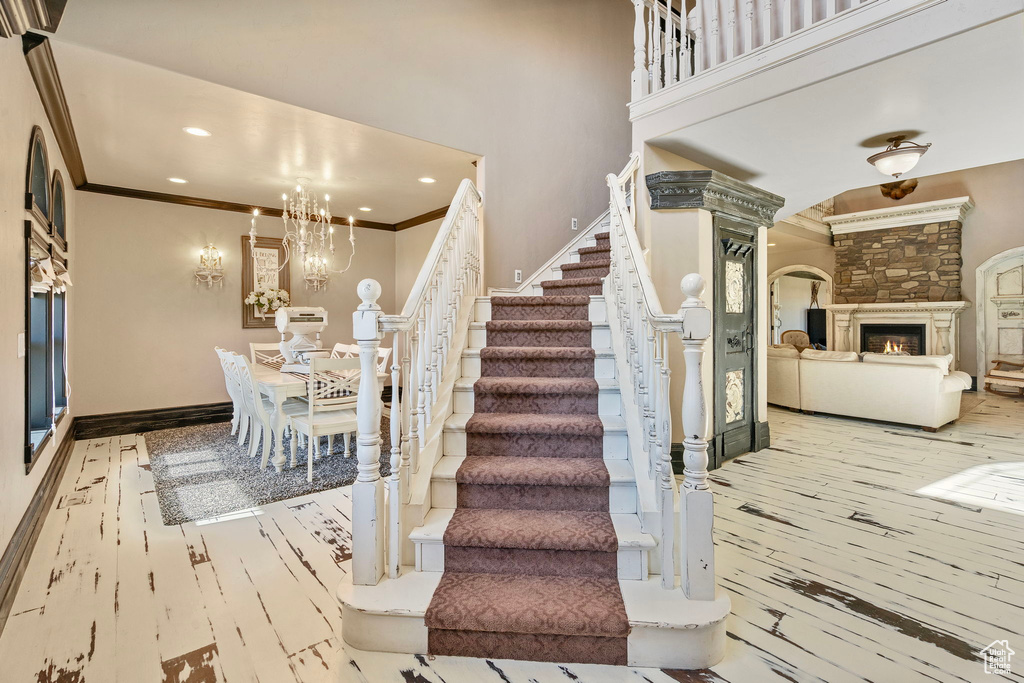 Stairs featuring a chandelier, a fireplace, baseboards, ornamental molding, and wood-type flooring