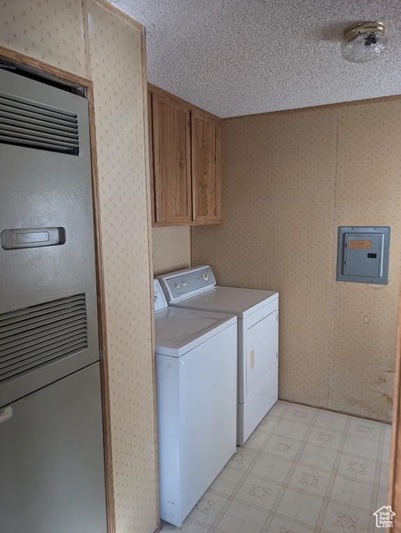 Laundry room with wallpapered walls, electric panel, washing machine and clothes dryer, a textured ceiling, and light floors