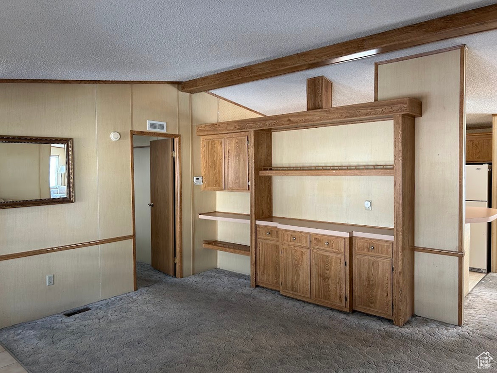 Interior space with lofted ceiling with beams, wood walls, visible vents, and a textured ceiling