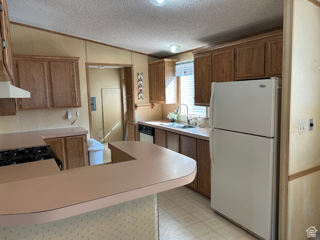 Kitchen with light floors, lofted ceiling, freestanding refrigerator, a sink, and wallpapered walls