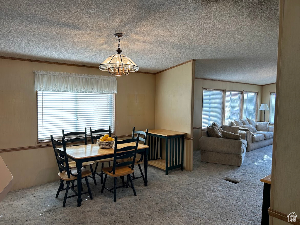 Carpeted dining space with a textured ceiling, ornamental molding, visible vents, and an inviting chandelier