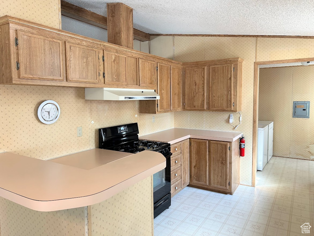 Kitchen with light floors, black gas stove, separate washer and dryer, under cabinet range hood, and wallpapered walls