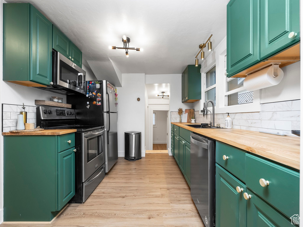 Kitchen featuring stainless steel appliances, butcher block counters, a sink, backsplash, and light wood finished floors