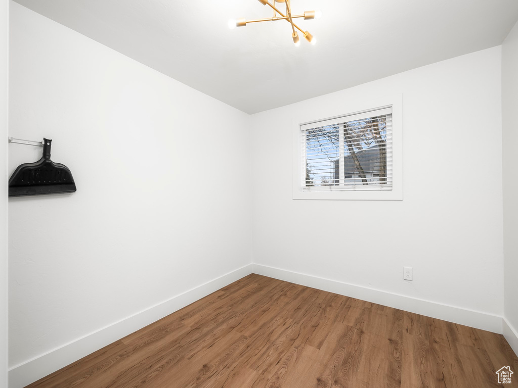 Unfurnished room with a chandelier, wood finished floors, and baseboards