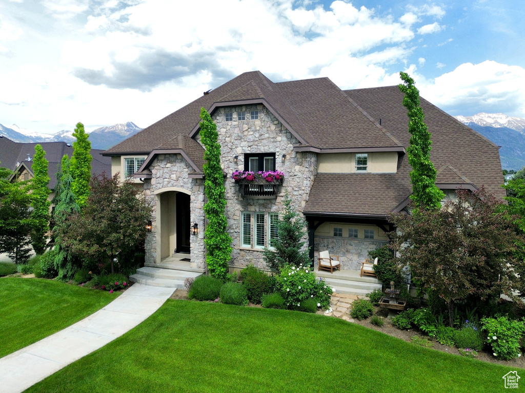 French country style house with stone siding, a front lawn, roof with shingles, and a mountain view