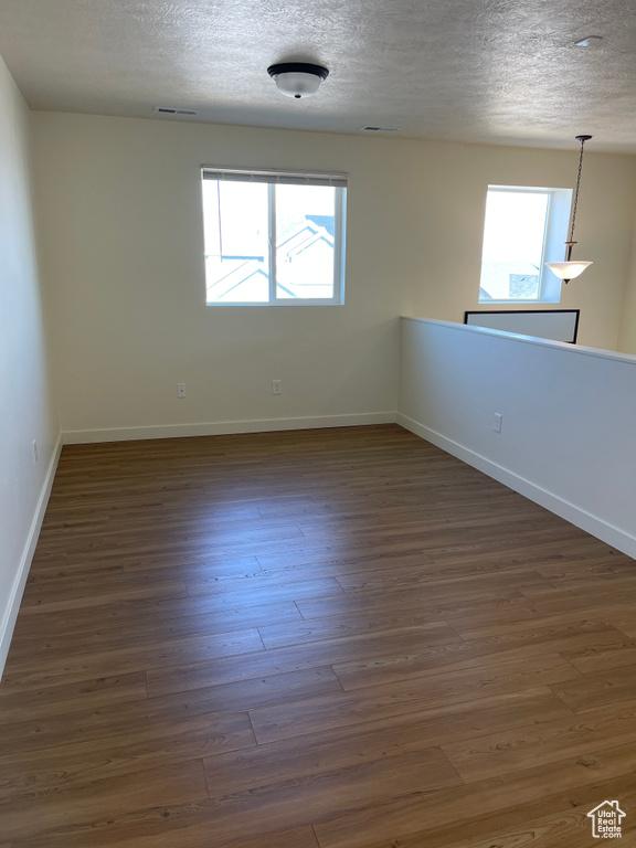 Unfurnished room with visible vents, baseboards, dark wood-style flooring, and a textured ceiling