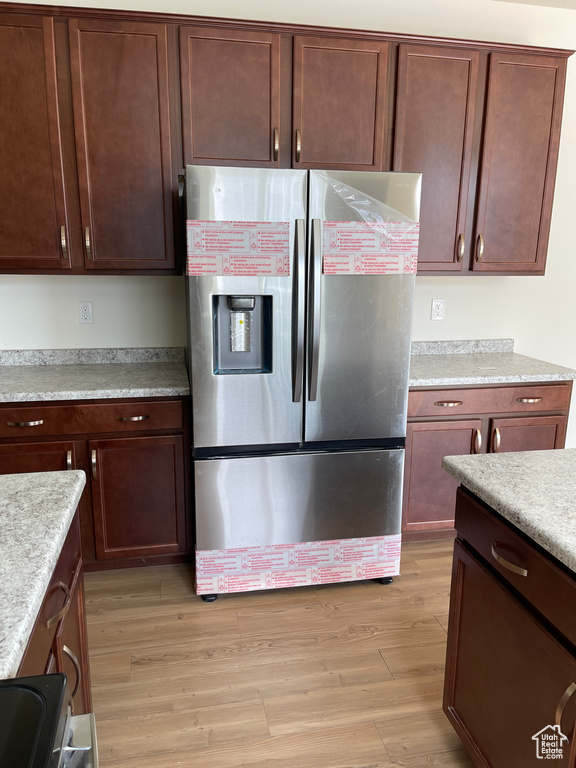Kitchen with light wood-style floors, dark brown cabinetry, light countertops, and stainless steel refrigerator with ice dispenser