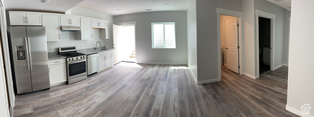 Kitchen featuring white cabinetry, appliances with stainless steel finishes, wood finished floors, under cabinet range hood, and baseboards