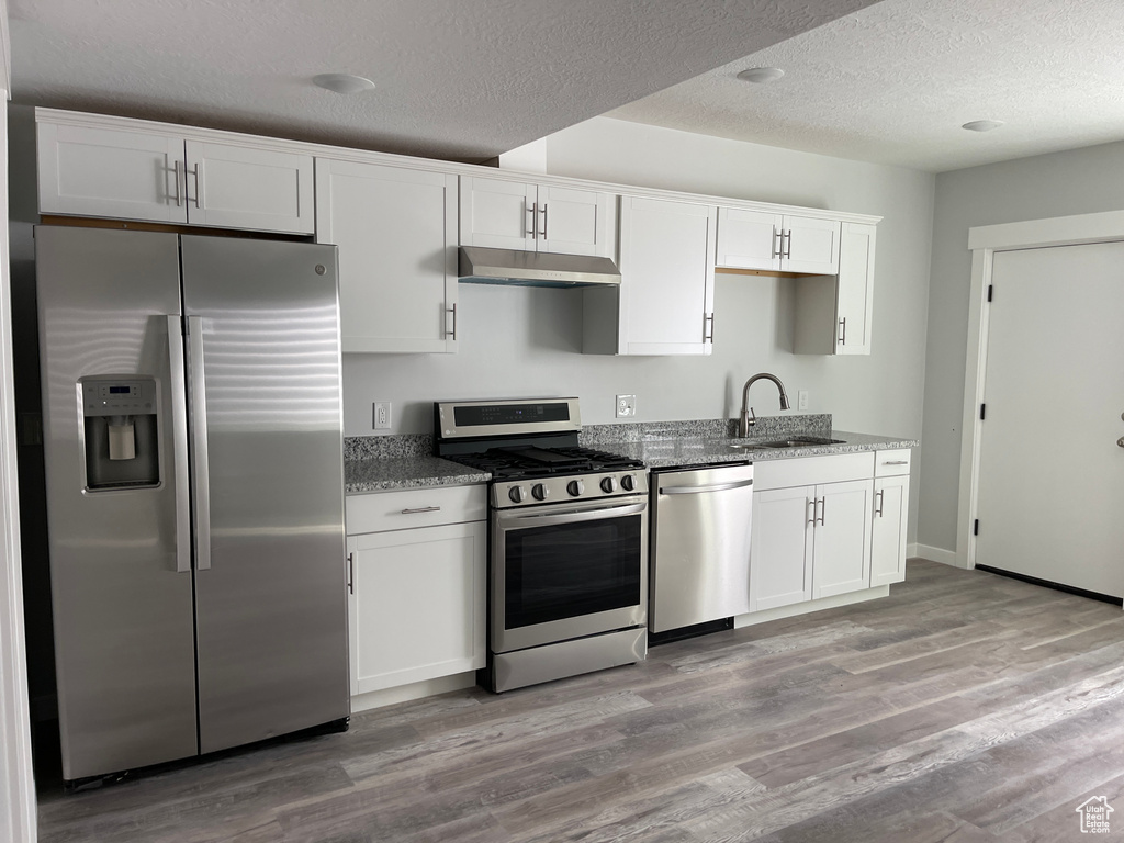 Kitchen featuring white cabinets, a sink, appliances with stainless steel finishes, under cabinet range hood, and stone countertops