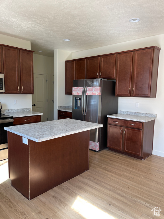Kitchen featuring light wood-type flooring, a textured ceiling, a center island, appliances with stainless steel finishes, and light countertops
