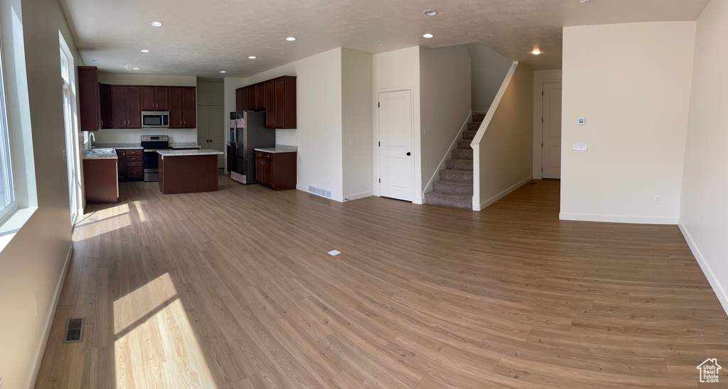 Unfurnished living room featuring visible vents, baseboards, light wood finished floors, recessed lighting, and stairs