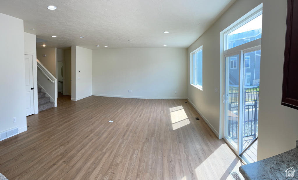 Unfurnished room featuring light wood-style floors, baseboards, visible vents, and stairway