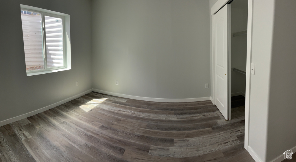 Unfurnished bedroom with a closet, dark wood-style floors, and baseboards