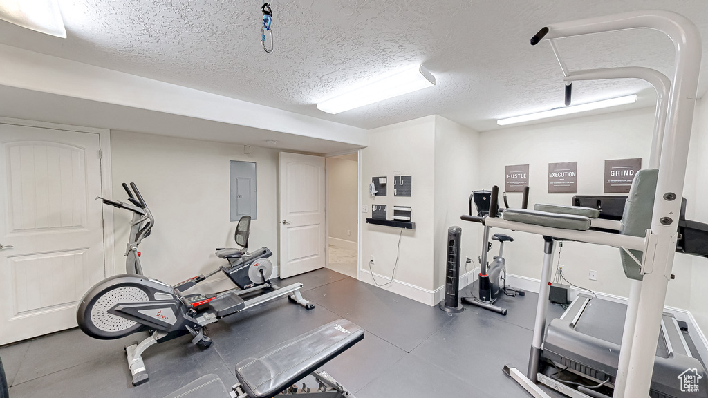 Exercise room featuring electric panel, baseboards, and a textured ceiling