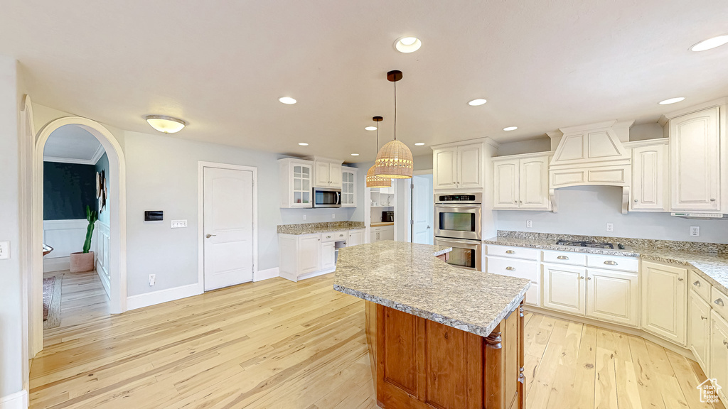 Kitchen with light wood finished floors, a kitchen island, premium range hood, appliances with stainless steel finishes, and arched walkways