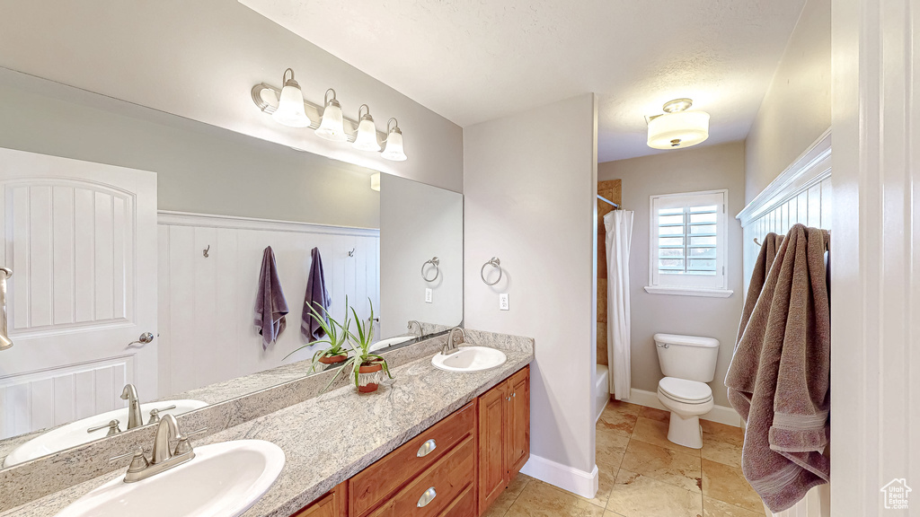 Full bathroom featuring a sink, shower / bath combo with shower curtain, toilet, and double vanity