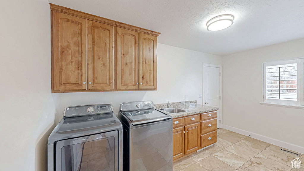 Clothes washing area with visible vents, washer and dryer, a sink, cabinet space, and baseboards