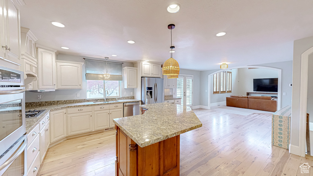 Kitchen with a center island, open floor plan, light wood-style floors, stainless steel appliances, and a sink