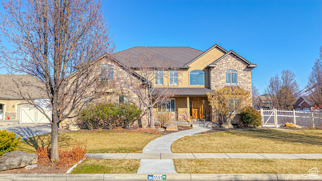 Traditional home with a front lawn, fence, stucco siding, stone siding, and an attached garage