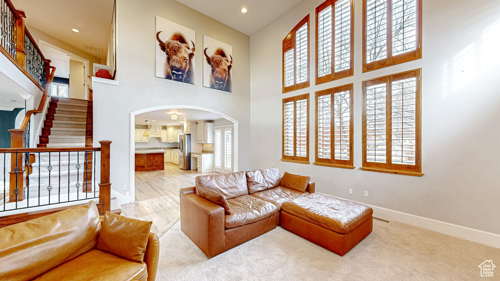 Living room featuring baseboards, a high ceiling, recessed lighting, arched walkways, and stairs