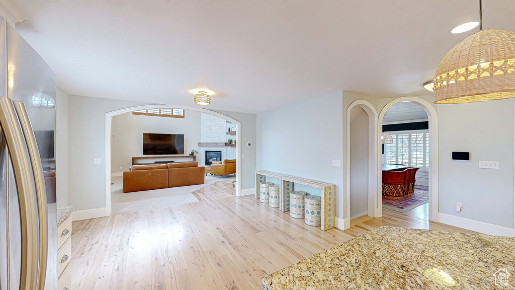 Unfurnished living room featuring a large fireplace, arched walkways, baseboards, and light wood finished floors