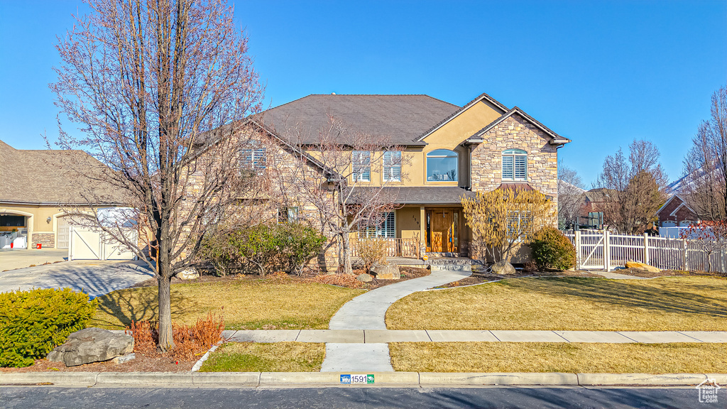 View of front of house with stone siding, stucco siding, a front lawn, and fence