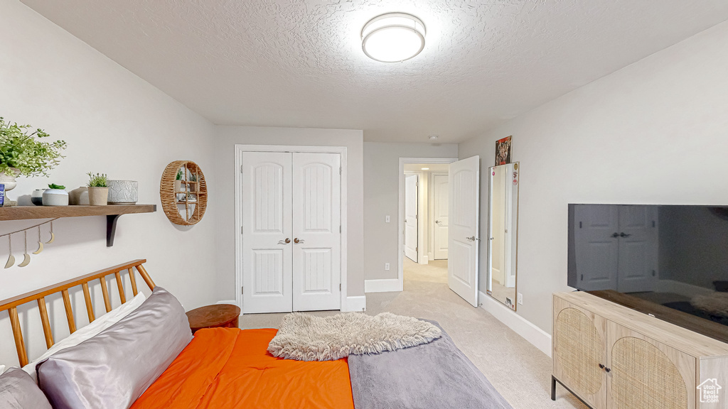 Bedroom featuring a closet, light carpet, a textured ceiling, and baseboards