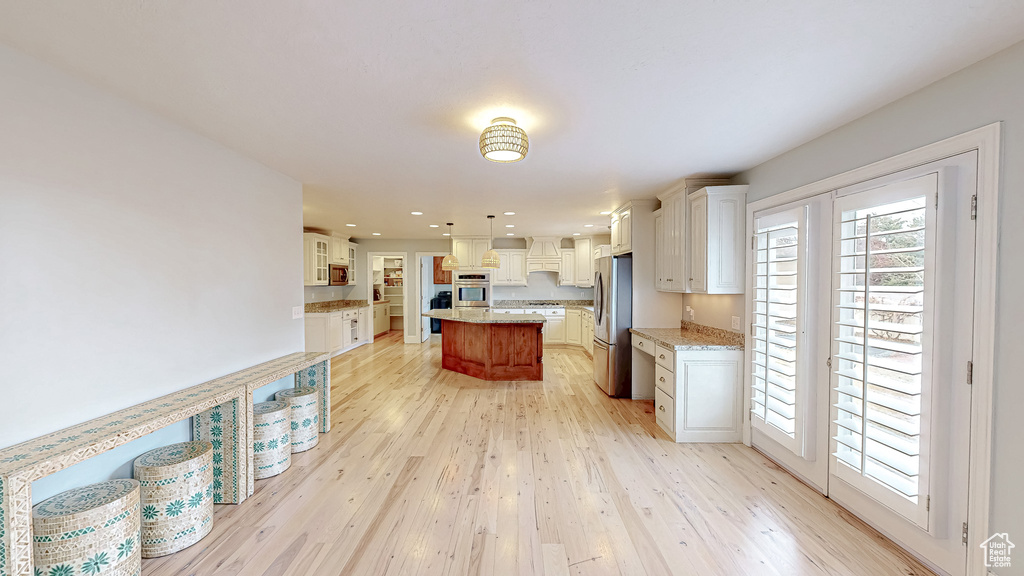 Kitchen featuring light wood finished floors, a center island, light stone counters, stainless steel appliances, and white cabinetry