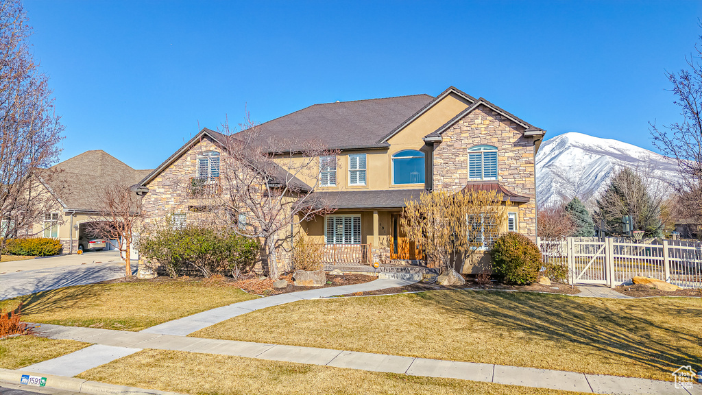 View of front facade with a front yard, fence, stucco siding, concrete driveway, and stone siding