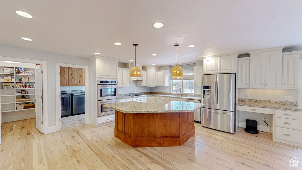 Kitchen with washer and clothes dryer, light wood-style flooring, stainless steel appliances, and a sink