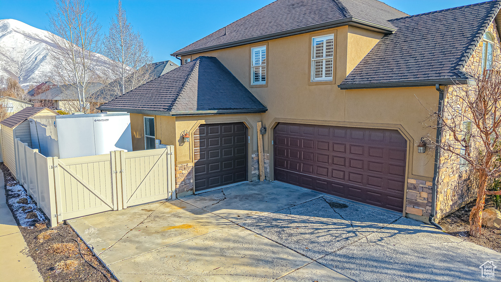 View of front of property featuring a gate, driveway, a shingled roof, stucco siding, and stone siding