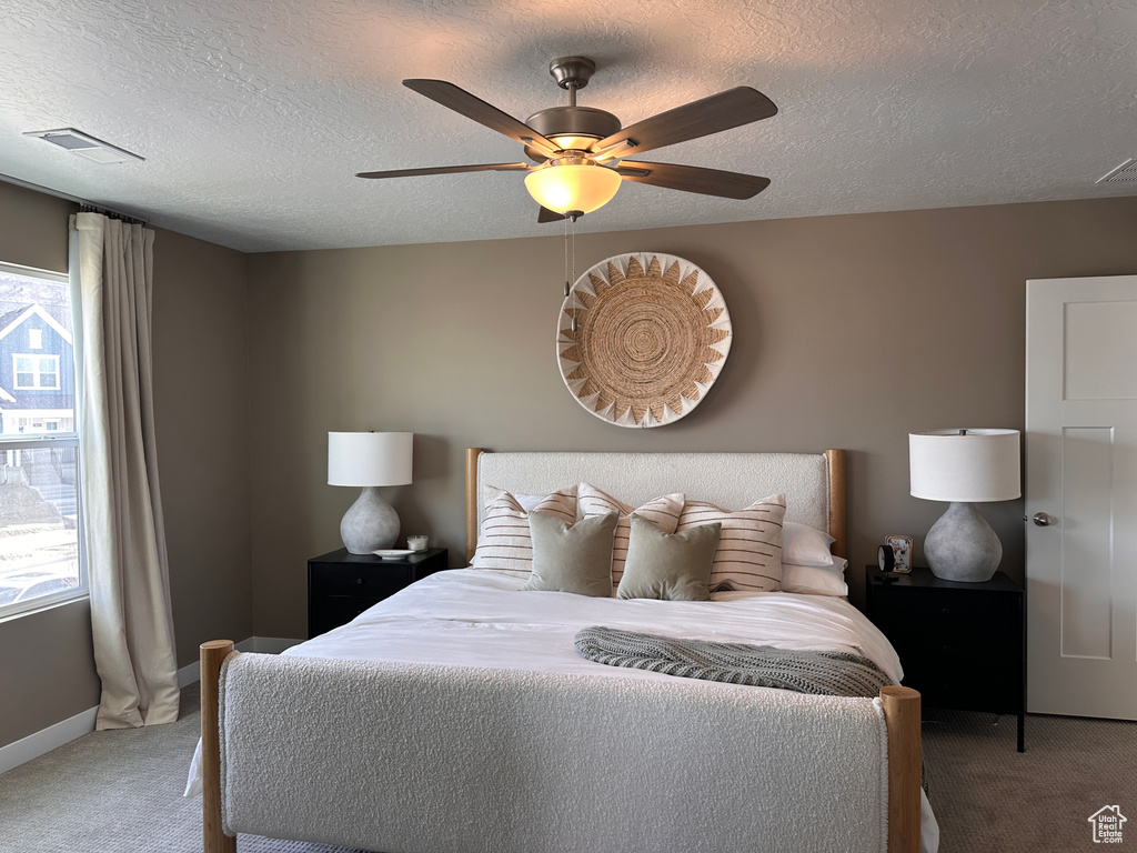 Carpeted bedroom with visible vents, a textured ceiling, baseboards, and a ceiling fan