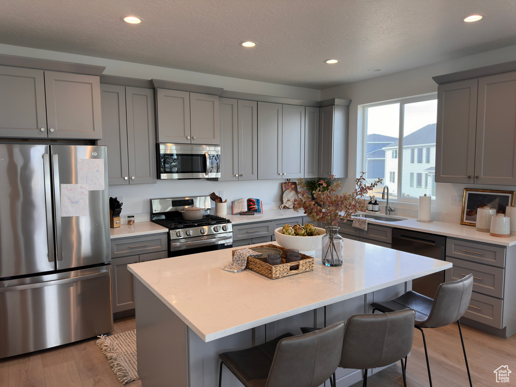 Kitchen featuring a breakfast bar area, light wood-style flooring, gray cabinetry, appliances with stainless steel finishes, and a center island