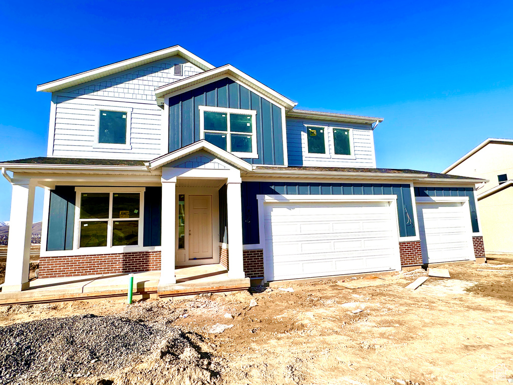 View of front of home featuring brick siding, board and batten siding, an attached garage, and a porch