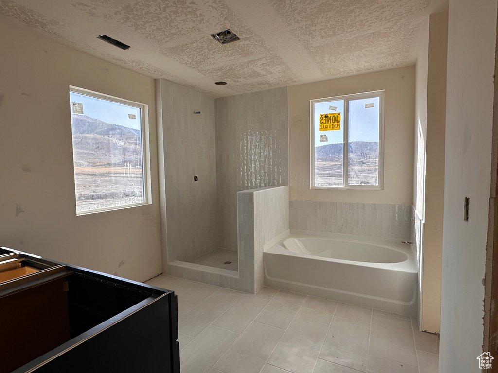 Full bath with tile patterned floors, a textured ceiling, a bath, and a shower stall