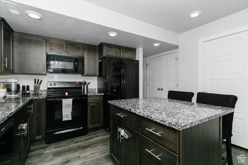 Kitchen with black appliances, dark wood-style floors, and stone counters