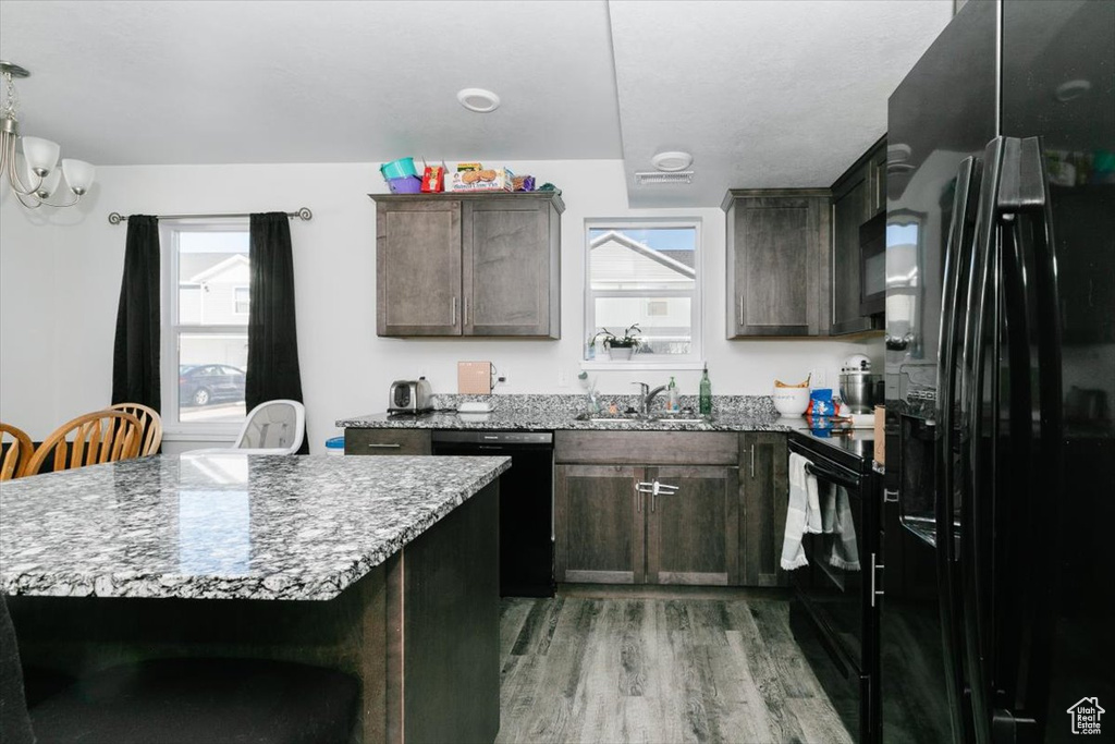 Kitchen featuring light stone counters, dark brown cabinetry, black appliances, and light wood-style floors