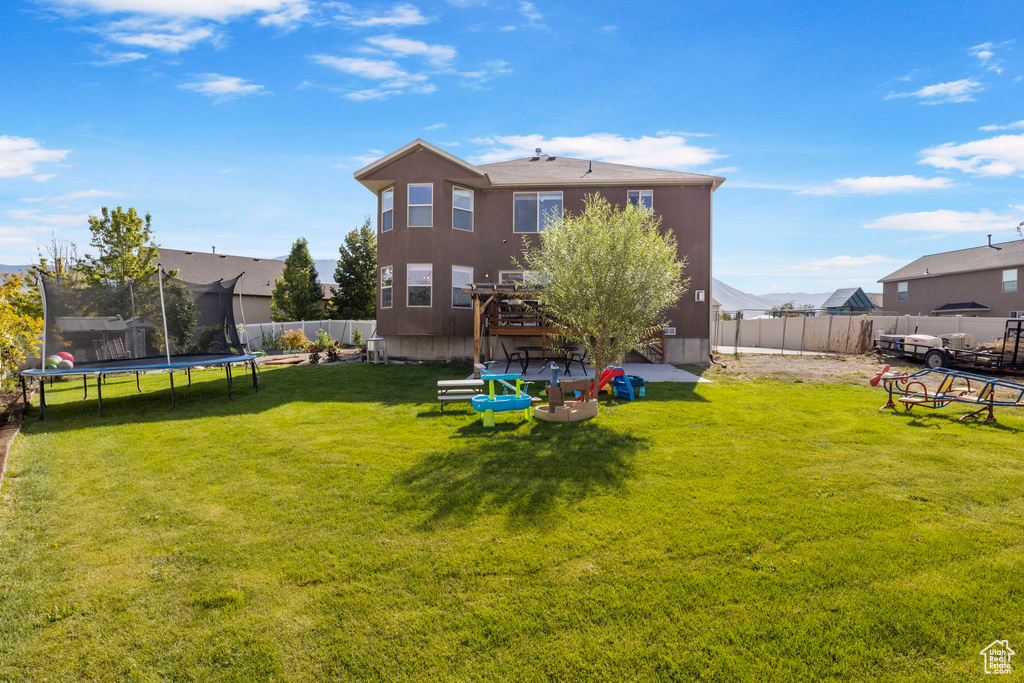 Back of house featuring a fenced backyard, a yard, and a trampoline