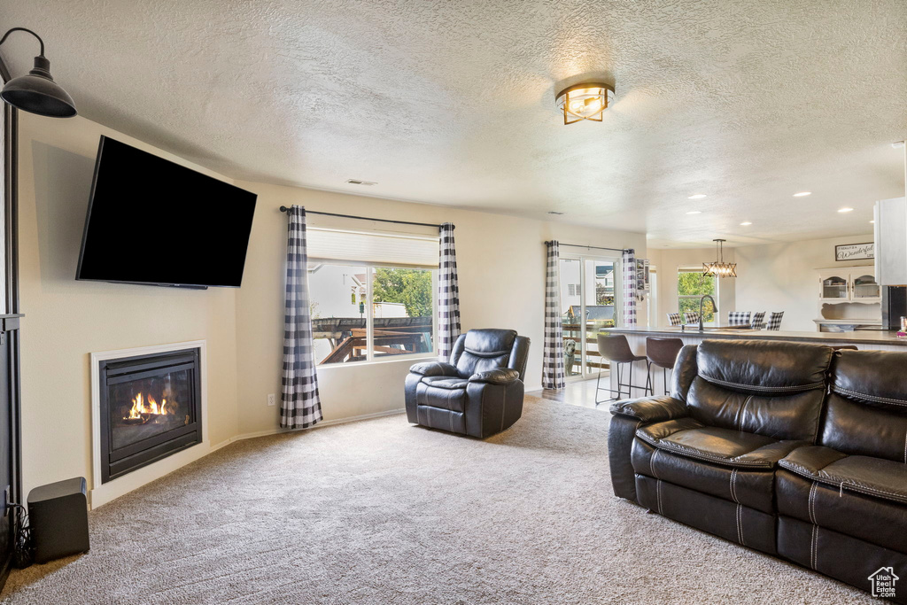 Carpeted living room featuring a textured ceiling, a glass covered fireplace, recessed lighting, baseboards, and a chandelier