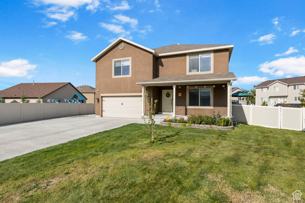 Traditional-style home featuring a front lawn, fence, concrete driveway, stucco siding, and a garage