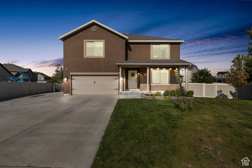 Traditional-style home with fence, stucco siding, a lawn, a garage, and driveway