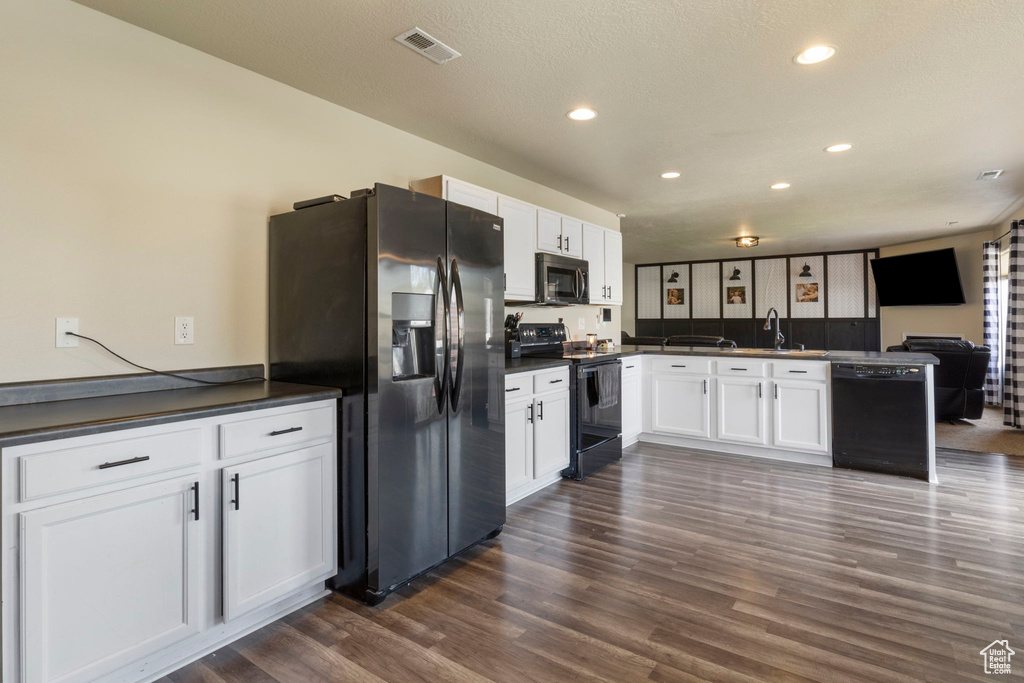 Kitchen with visible vents, black appliances, dark countertops, a peninsula, and white cabinets