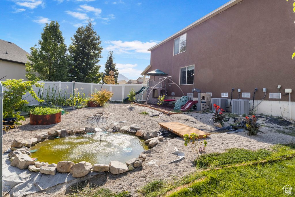 View of yard with fence, a garden, a small pond, a playground, and central air condition unit