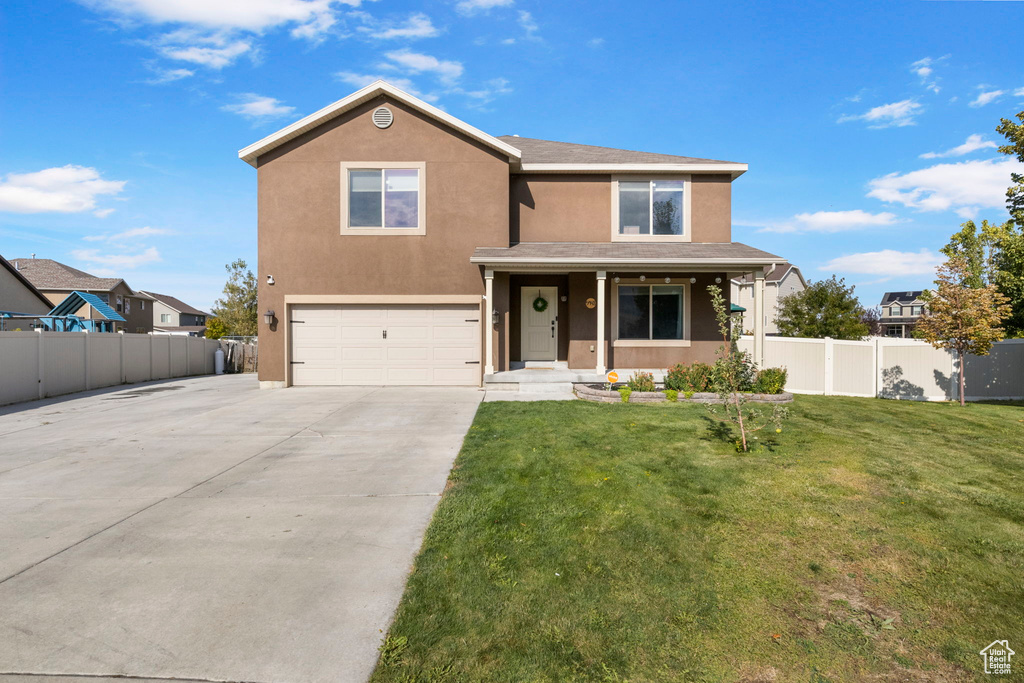 Traditional home with stucco siding, fence, concrete driveway, a front yard, and an attached garage