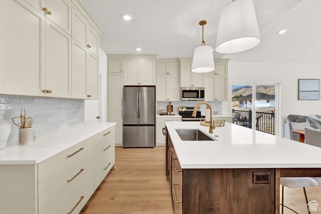 Kitchen with decorative backsplash, light wood-type flooring, appliances with stainless steel finishes, and a sink