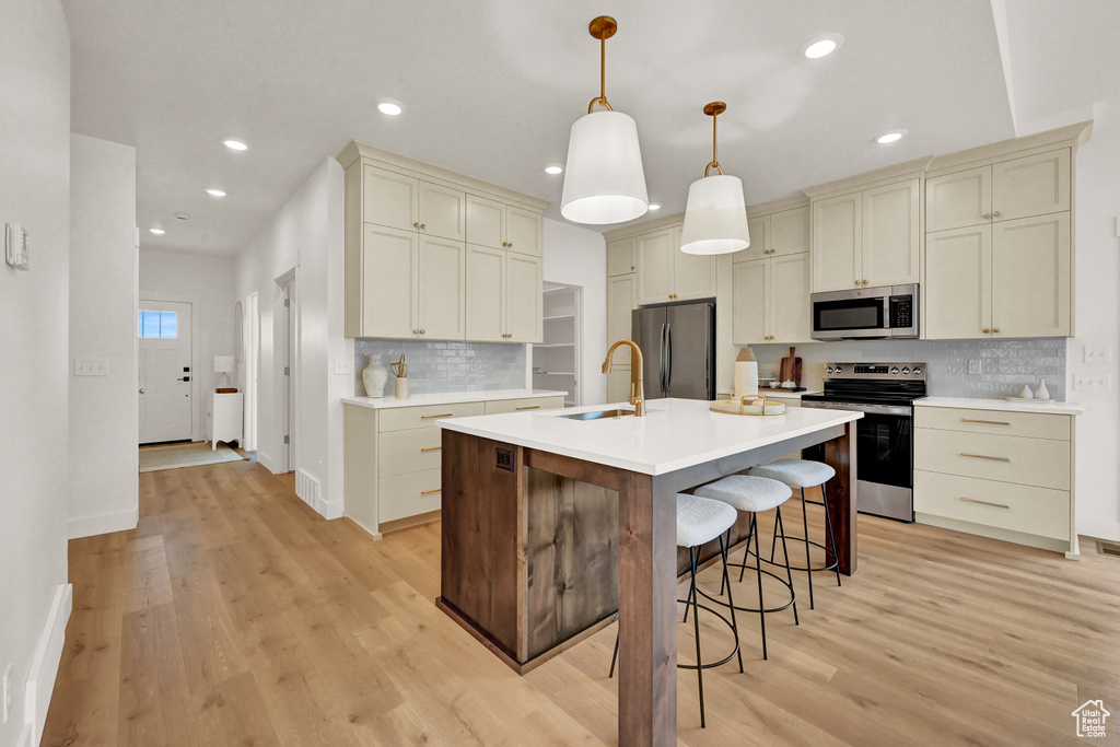 Kitchen featuring light wood finished floors, a breakfast bar, a sink, decorative backsplash, and appliances with stainless steel finishes