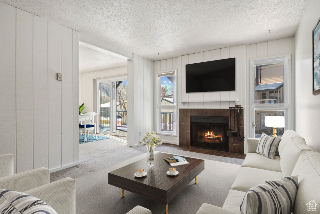 Living area featuring carpet floors, a tiled fireplace, a textured ceiling, and wood walls