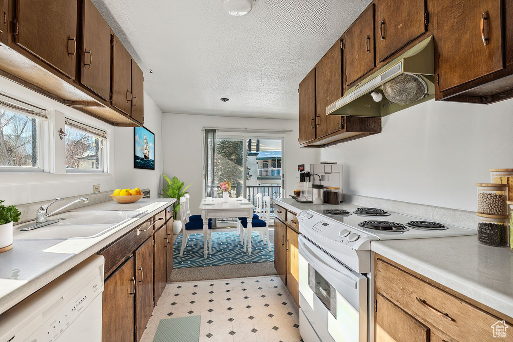 Kitchen with white appliances, under cabinet range hood, light countertops, a sink, and a textured ceiling