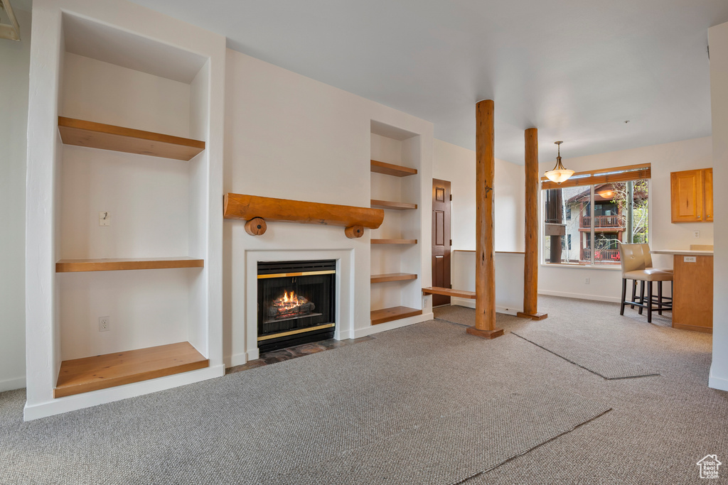 Unfurnished living room featuring carpet flooring, a fireplace with flush hearth, built in features, and baseboards