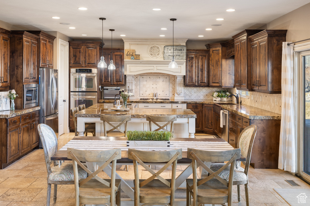 Kitchen featuring visible vents, an island with sink, backsplash, stone tile flooring, and appliances with stainless steel finishes